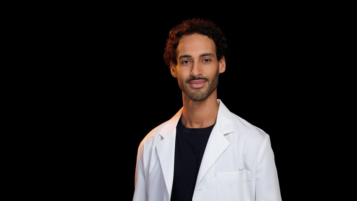 Medical professional wearing a white lab coat against a black background.